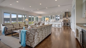 A spacious living area with a sofa, coffee table, and chairs, a kitchen with modern appliances, and large windows offering a view of the outdoors.