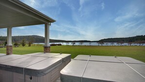 A covered outdoor area with two hot tubs, a grassy lawn, and a lake in the background.