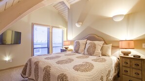 Een slaapkamer met een groot bed, twee bedlampen, een nachtkastje en een aan de muur bevestigde televisie.
