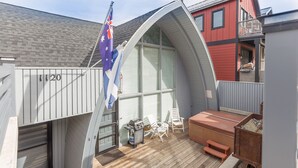 Een overdekt terras buiten met een barbecue, zithoek en een vlag.