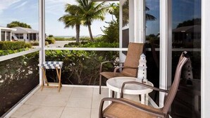 En balkon med to stole, et lille bord og udsigt til en palme og strand.