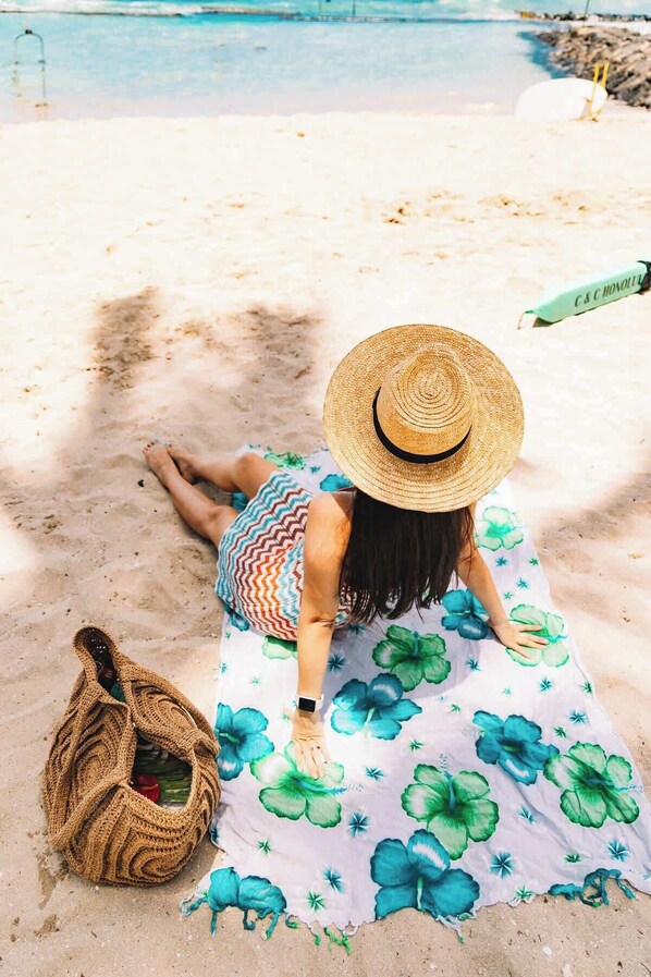 A person lying on a beach towel with a floral pattern, a straw hat, and a woven bag.
