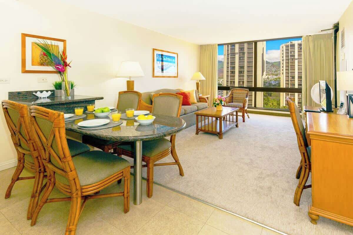 Une chambre d’hôtel moderne dotée d’un coin repas, d’un canapé et d’un balcon offrant une vue sur la ville.