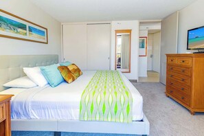 Une chambre à coucher comprenant un lit, une commode, un téléviseur et une porte donnant sur une autre pièce.