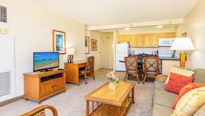 A compact living space with a television, wooden furniture, a kitchen area, and a dining table. - 1BR condo w/ lanai & pool access (Honolulu)