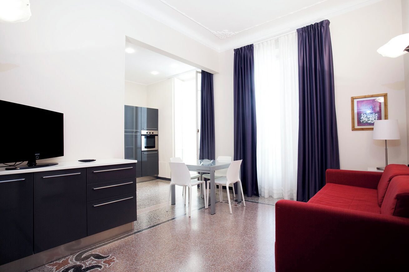 A modern hotel room with a dining area, a red sofa, and a flat-screen TV.