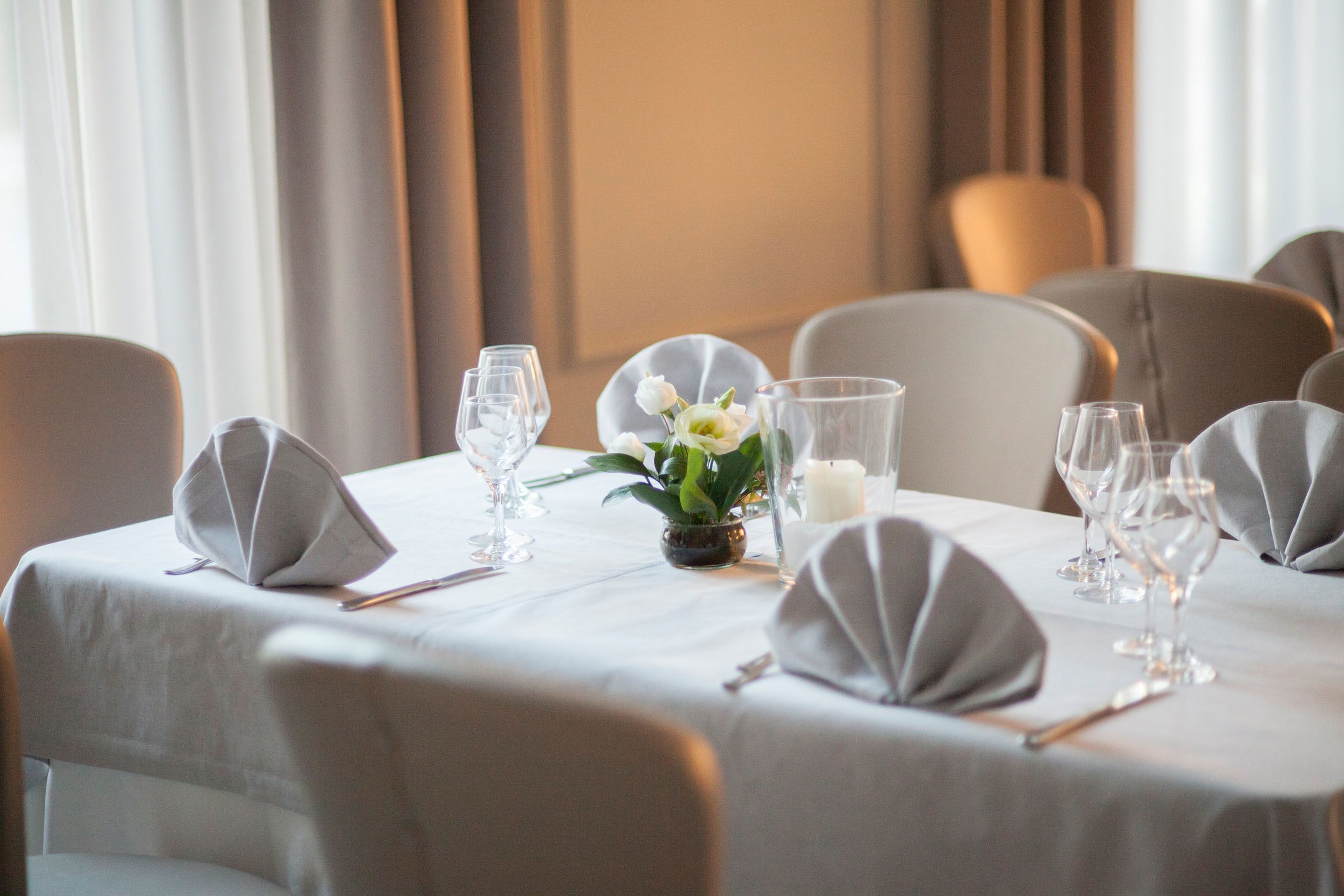 A dining table set with white tablecloth, glassware, and a small vase with white flowers.