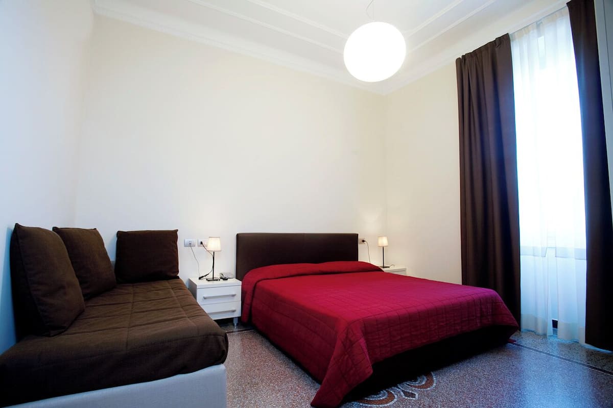 A hotel room with a bed, a nightstand, a lamp, and a window with curtains.