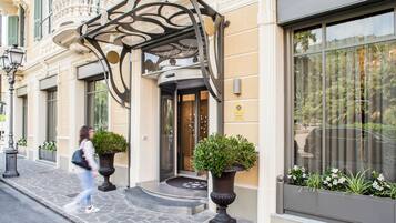 A building entrance with a curved metal canopy, a stone-paved entrance, and potted plants.