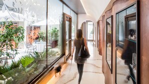 A modern hotel corridor with glass walls, a reflective floor, and a view of an outdoor dining area with plants and chairs. - Hotel Dei Fiori (Alassio)