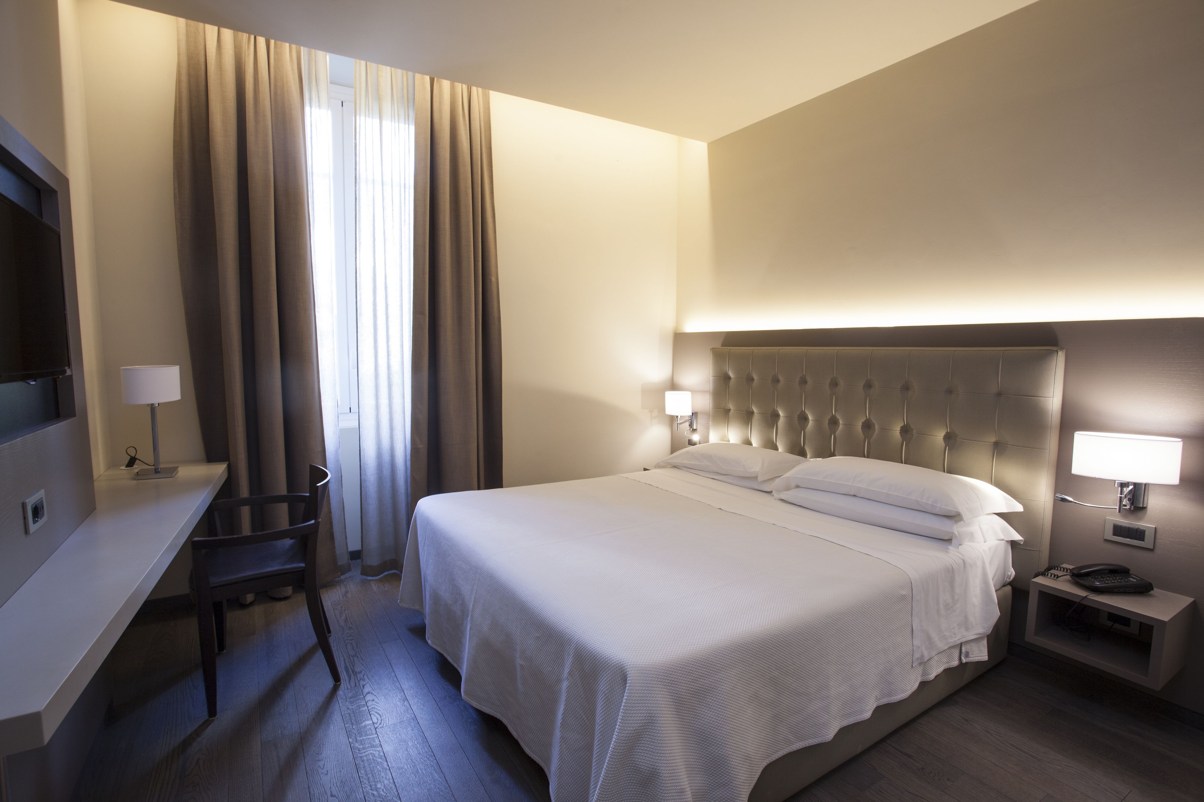 Una habitació d'hotel amb un llit gran, un escriptori, una cadira, una tauleta de nit i una televisió.