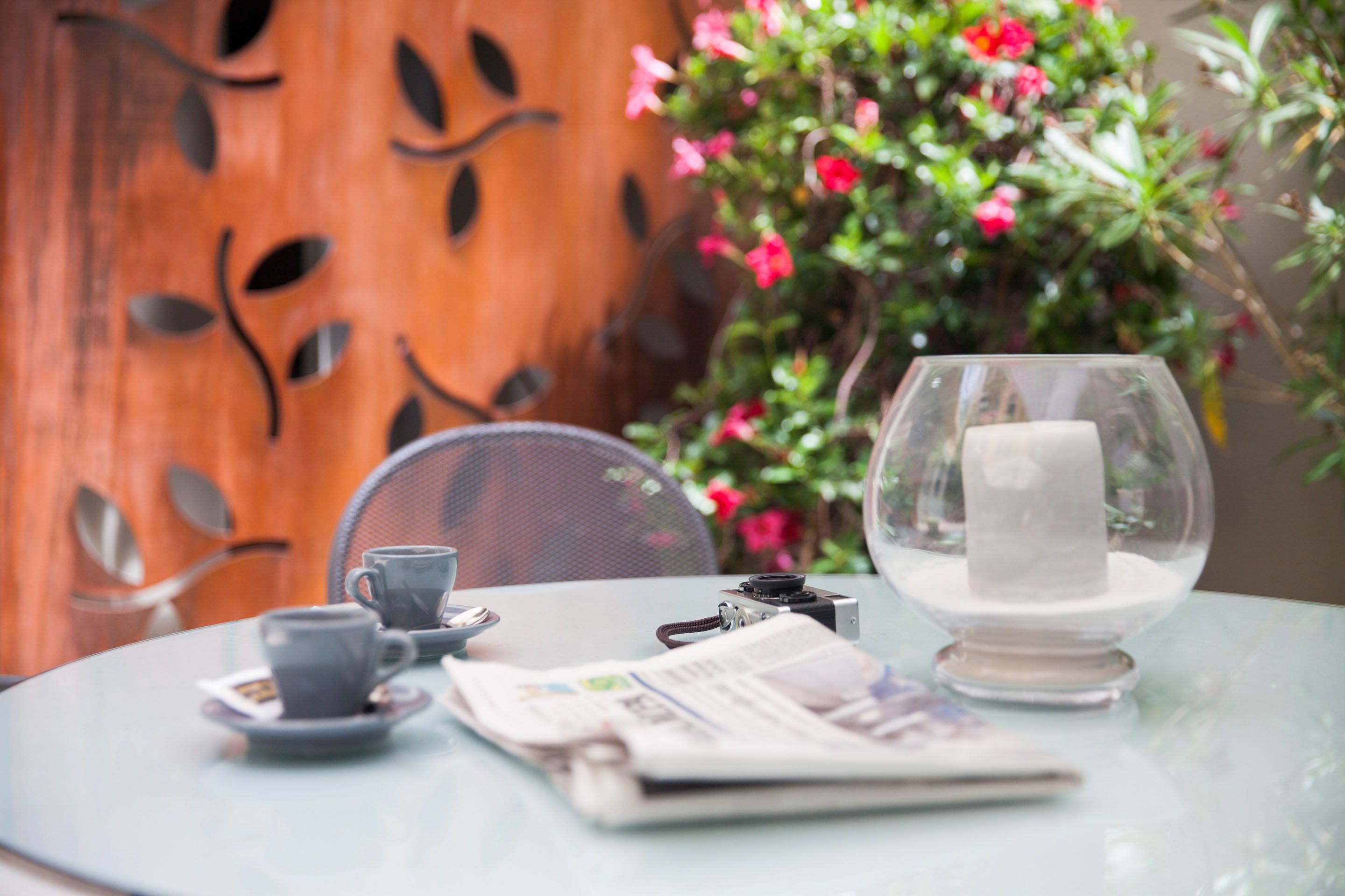 A round glass table with a newspaper, a cup, saucer, and a camera.