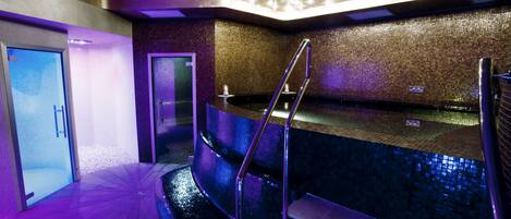 A modern indoor pool area with a glass door entrance, a metal ladder, and a tiled wall.