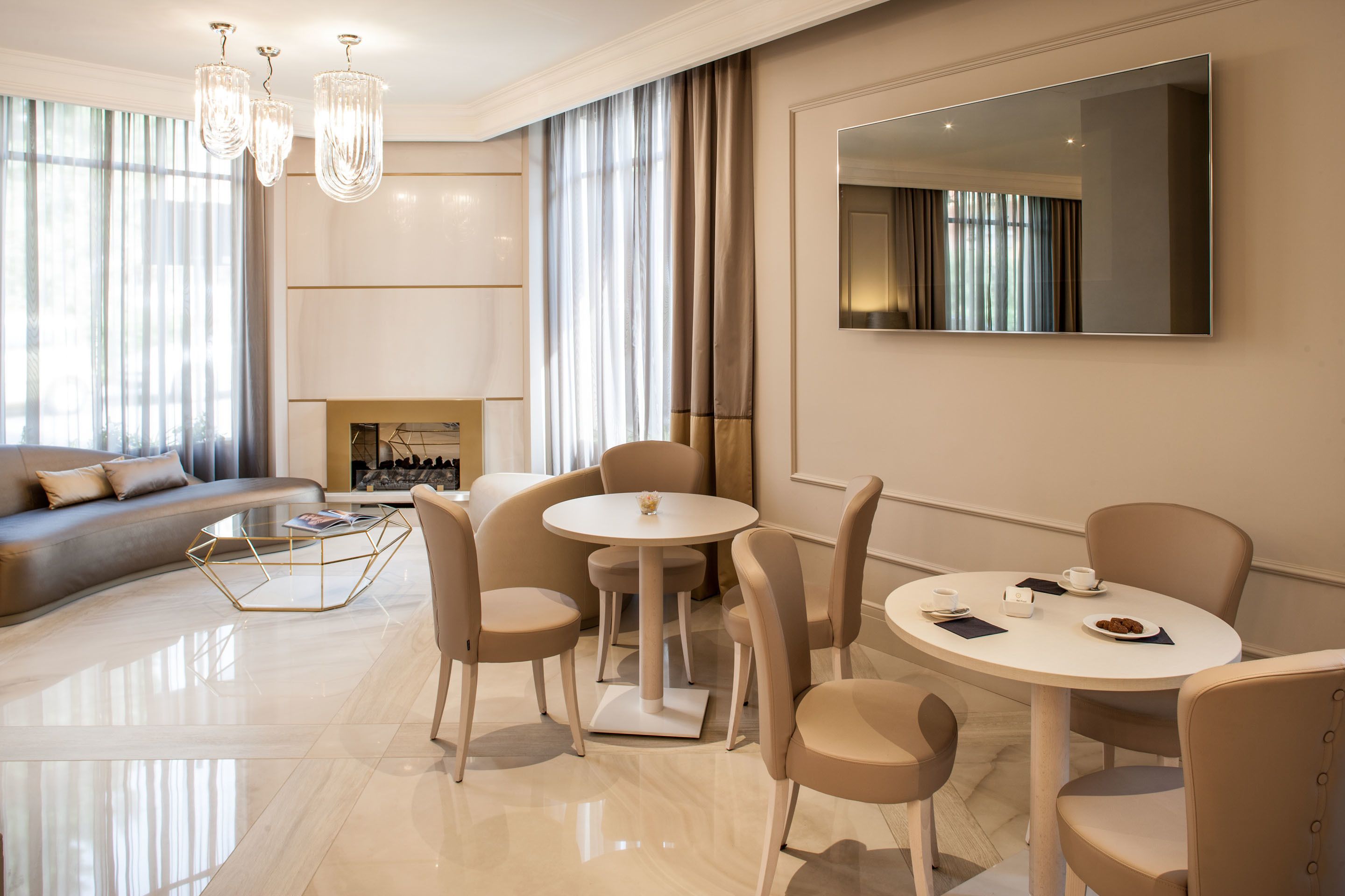 Une chambre d’hôtel moderne comprenant un coin salon, une table à manger avec des chaises, un grand miroir et une cheminée.