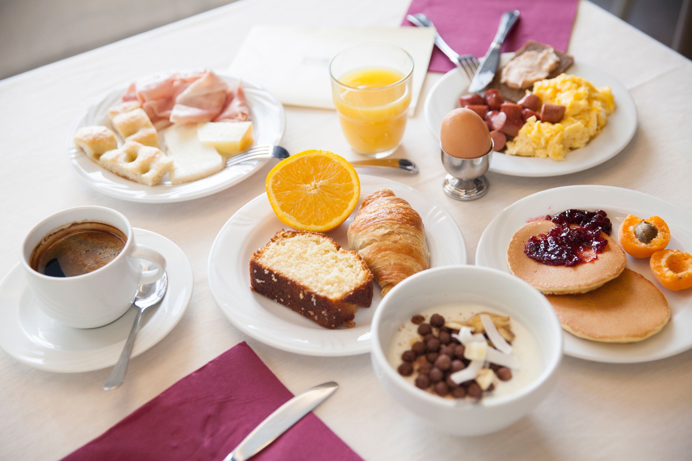 A breakfast table with plates of food, a glass of orange juice, a cup of coffee, and a croissant.