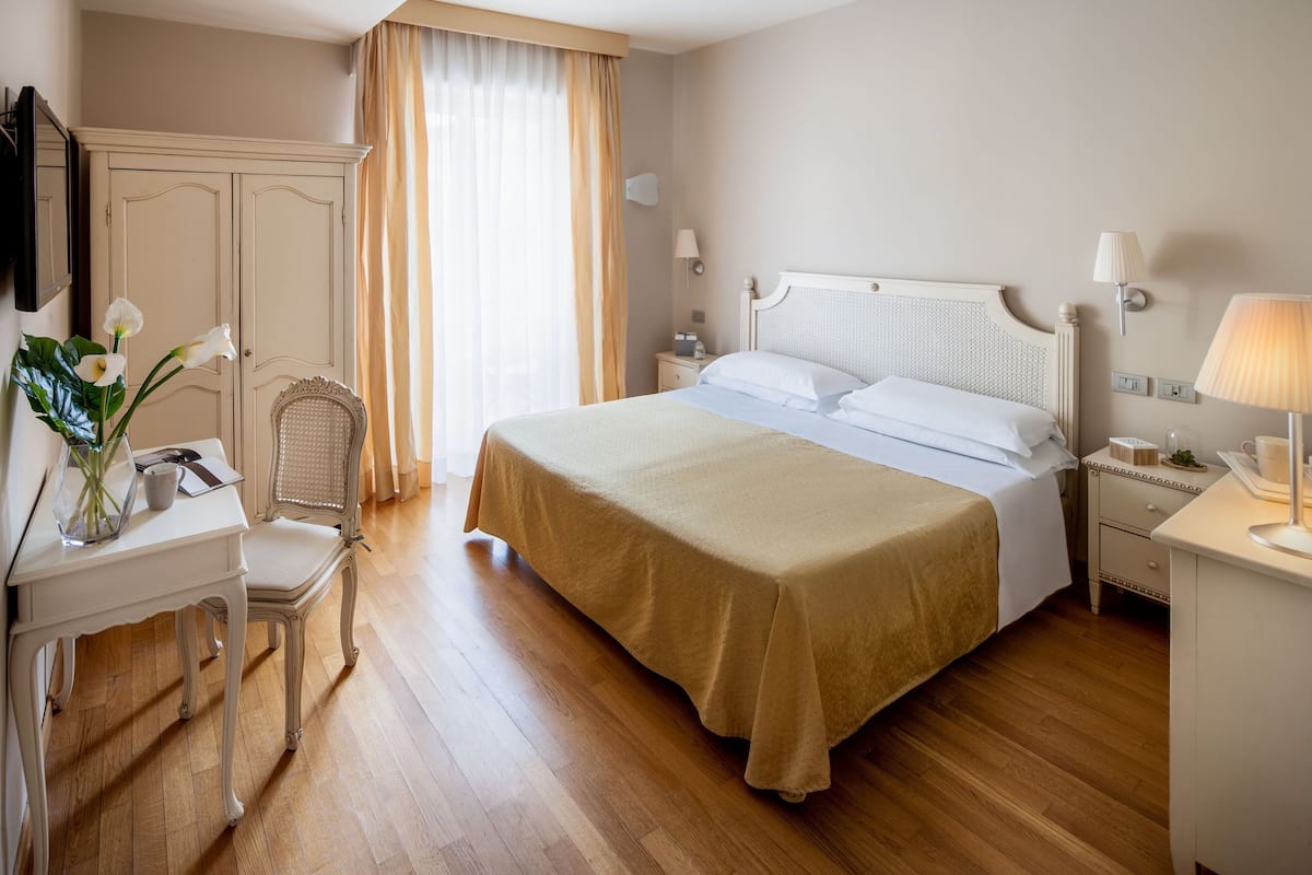 A hotel room with a large bed, a desk, a chair, a wardrobe, and a window with curtains.