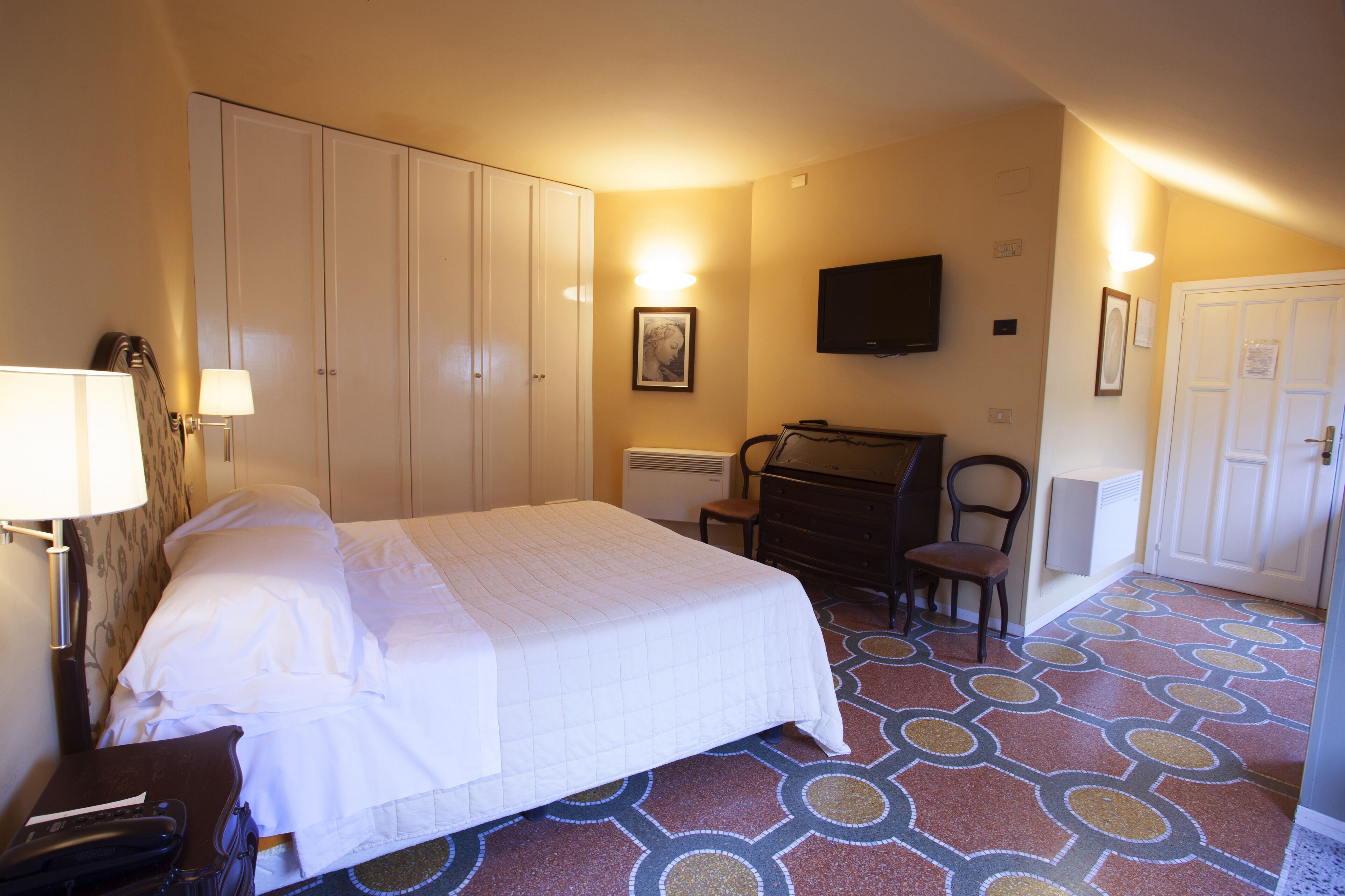 A hotel room with a bed, wardrobe, desk, chair, and a flat-screen TV.