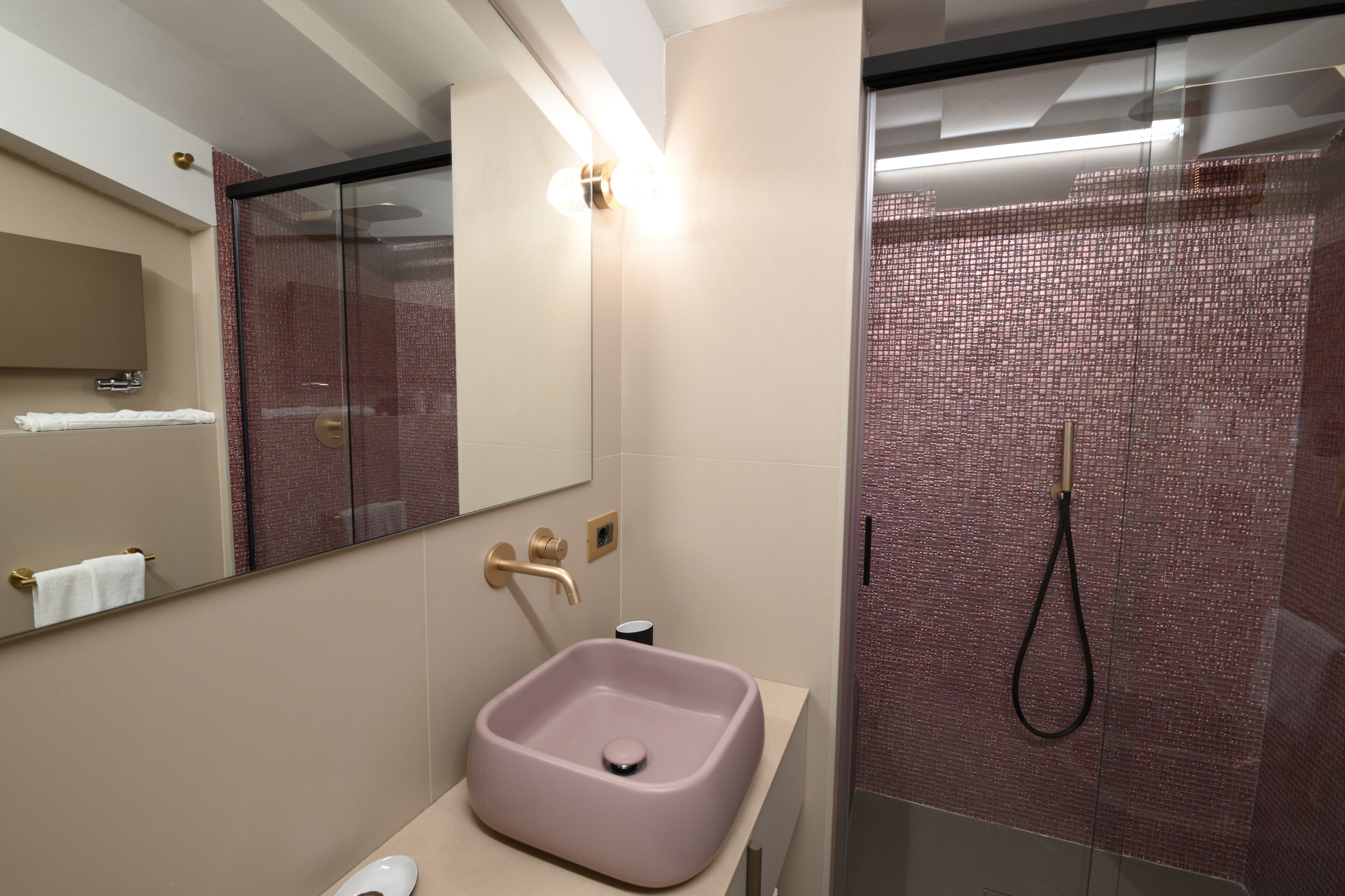 Un baño moderno con un lavamanos rosa, una ducha con cerramiento de vidrio y un espejo grande.