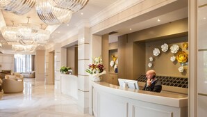 A hotel reception area with a modern design, featuring a marble floor, elegant chandeliers, and a reception desk with a vase of flowers. - Hotel Dei Fiori (Alassio)
