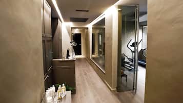 Corredor moderno de hotel com área de toucador, esteira e porta de vidro que dá para um quarto.