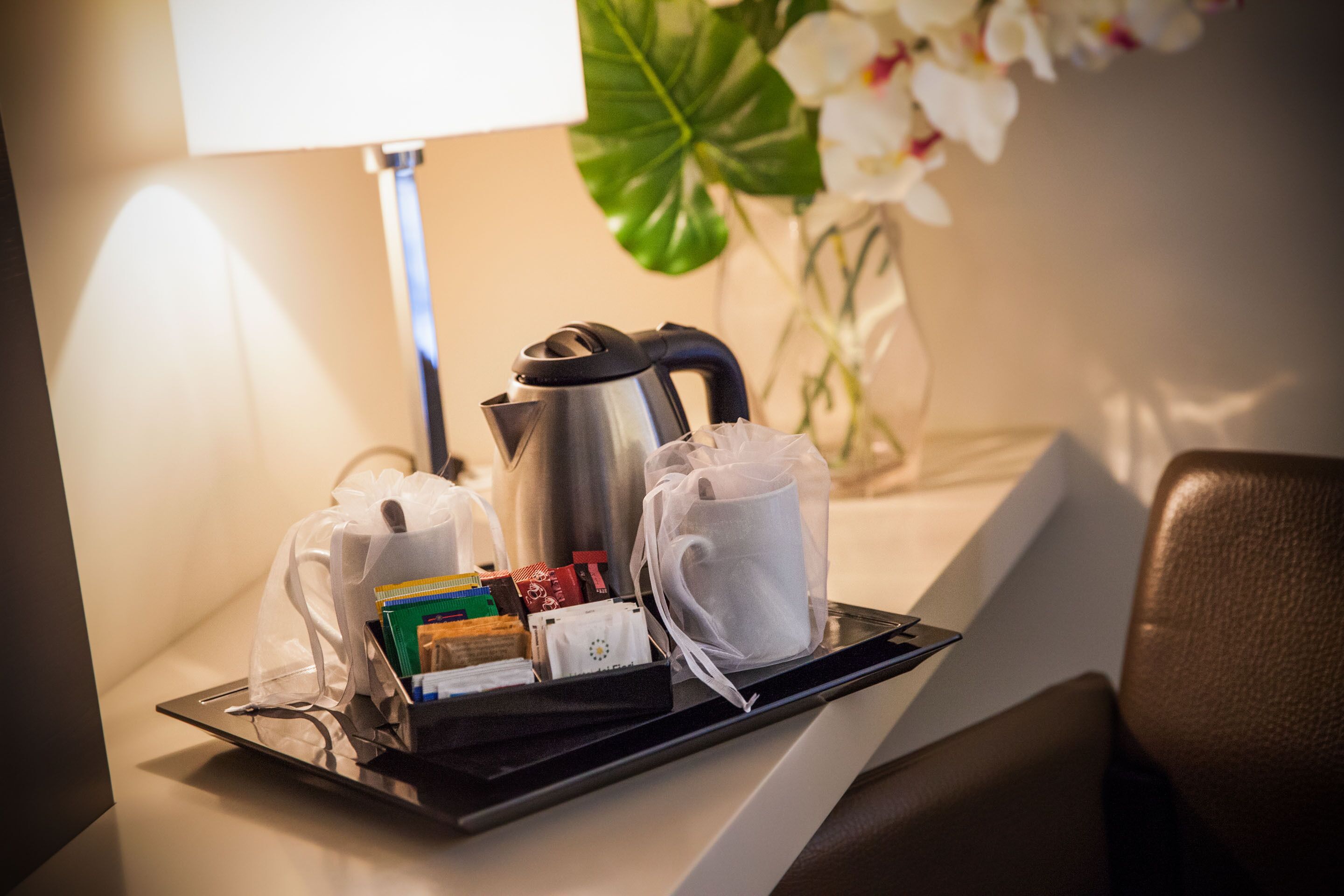 A tray with a kettle, teapot, and cups, along with some toiletries and a small box, on a hotel counter.