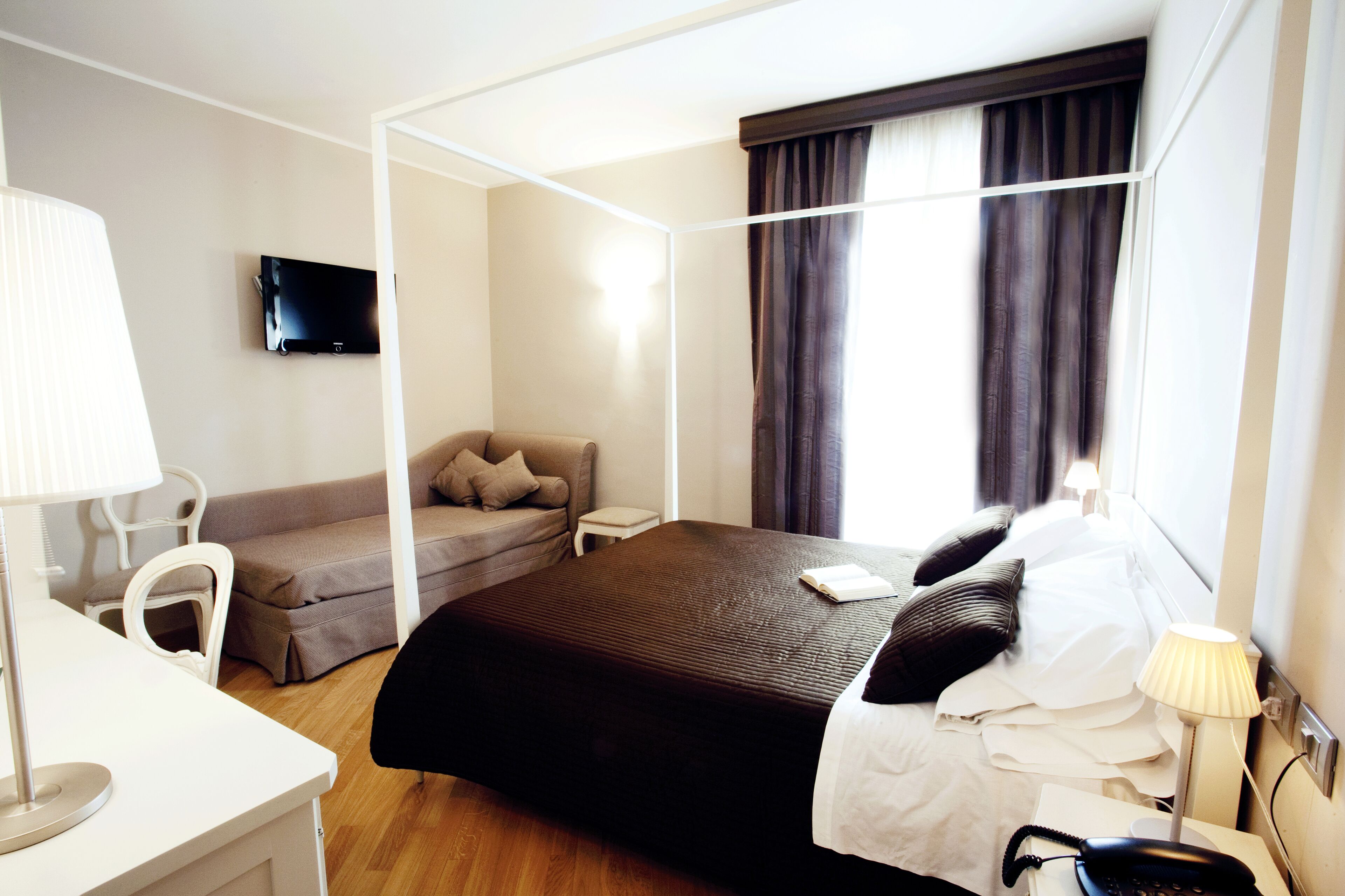 Camera d'albergo con un letto, una scrivania, una sedia, una televisione e una finestra con tende.