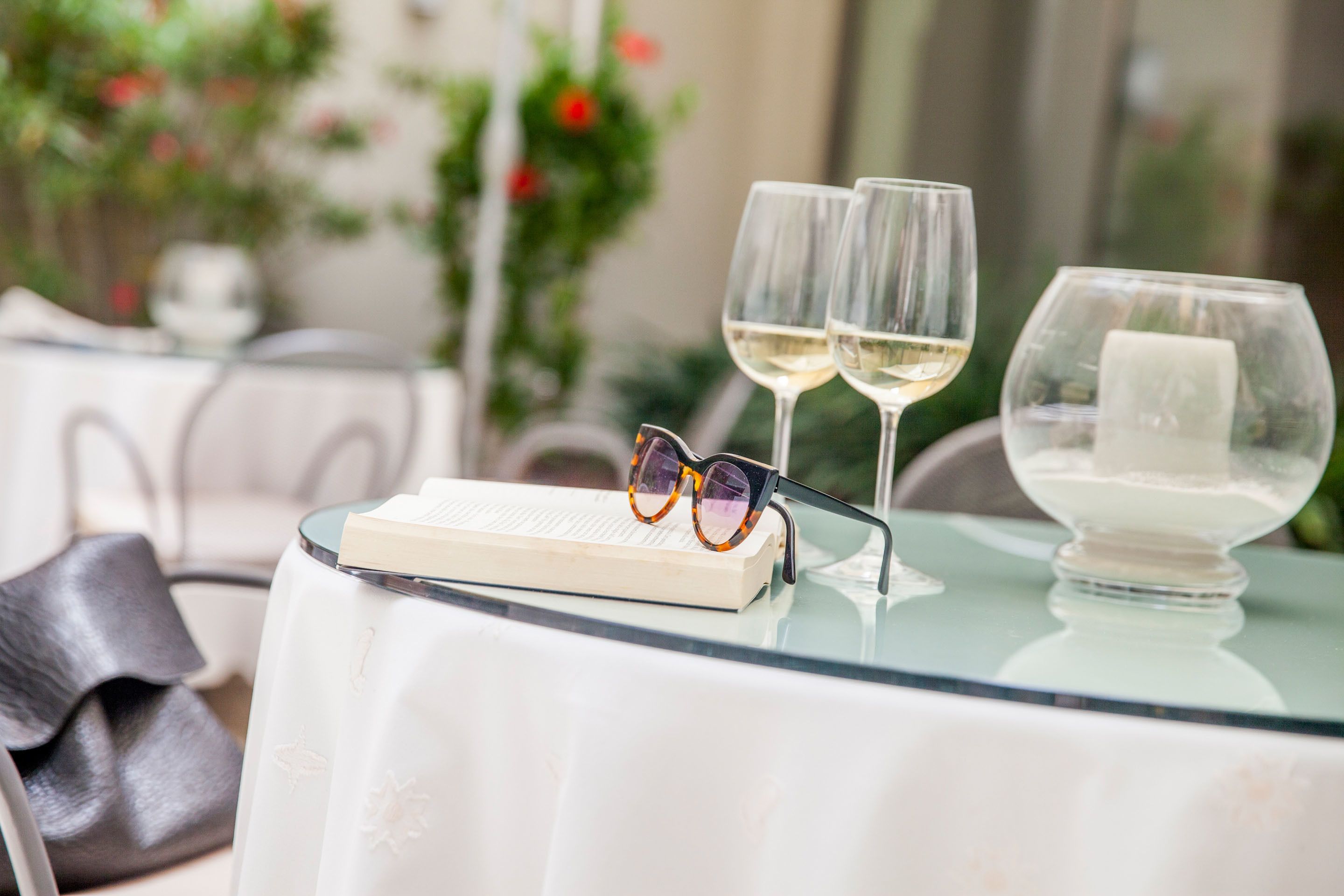 Ein Tisch mit zwei Weingläsern, einem Buch und einem Brillenpaar darauf.