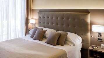 A hotel room with a large bed, a headboard, a nightstand with a lamp, and a bedside table with a book and a container.