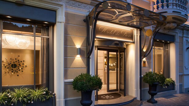 A hotel entrance with a glass door, a decorative metal canopy, and two potted plants. - Hotel Dei Fiori (Alassio)