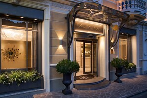 A hotel entrance with a glass door, a decorative metal canopy, and two potted plants. - Hotel Dei Fiori (Alassio)