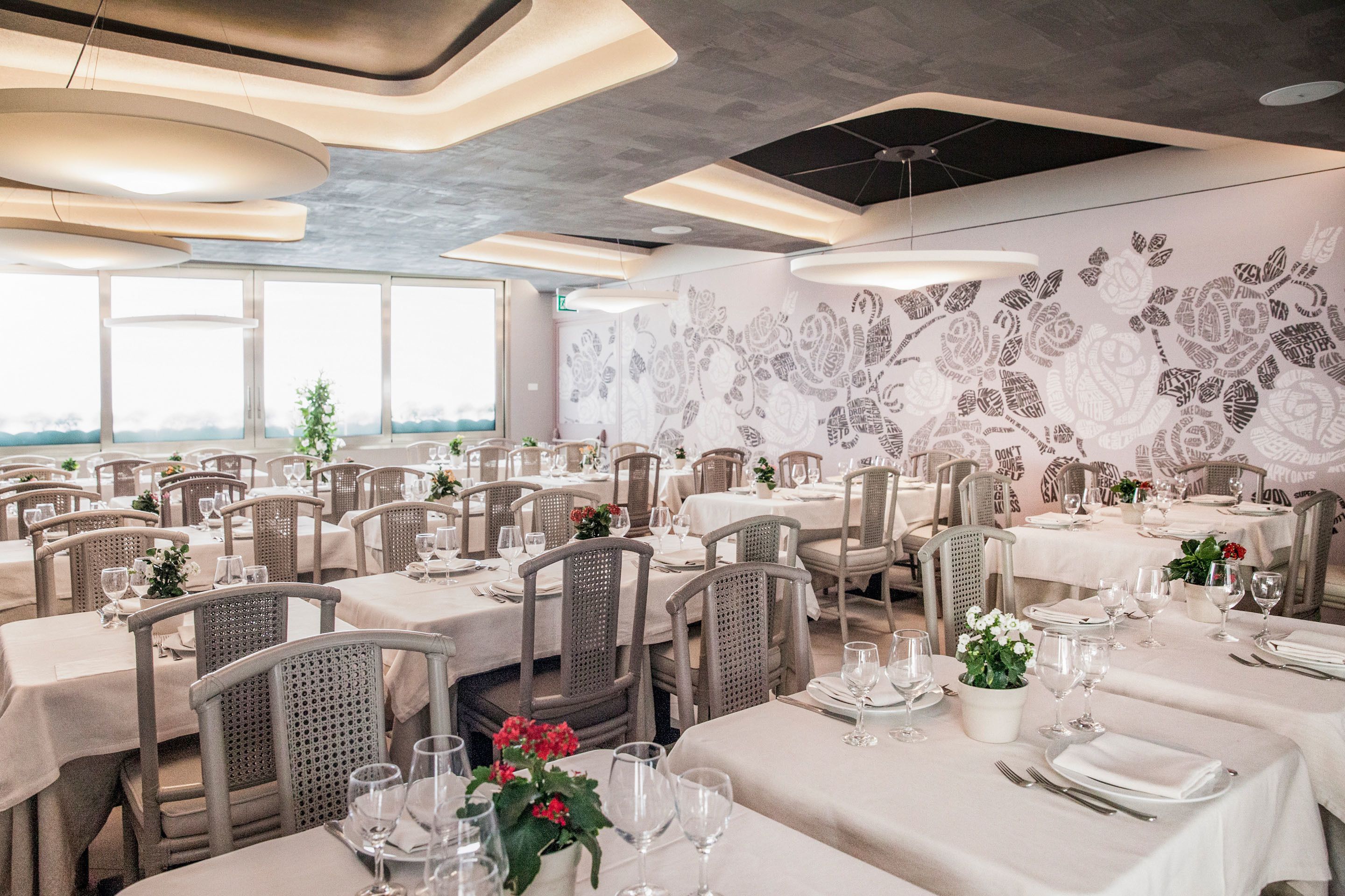 Un restaurante con varias mesas dispuestas para comer, que destaca un diseño moderno en el techo y un mural floral en la pared.