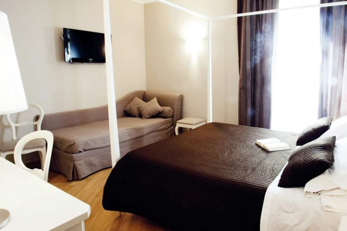 A hotel room with a bed, a sofa, a TV, and a desk.