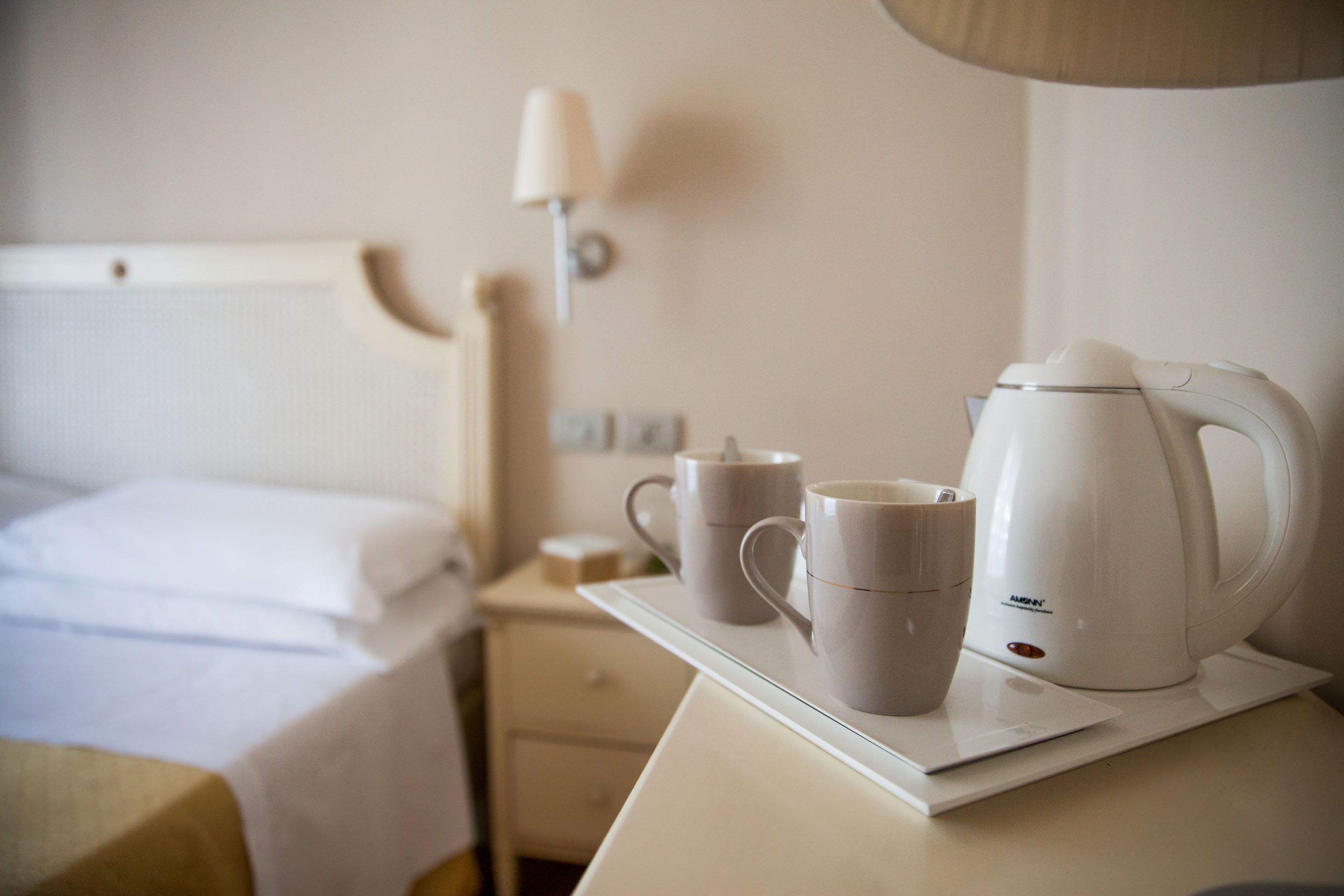 A hotel room with a neatly made bed, a bedside table with a lamp, and a tray with two cups and a coffee maker.