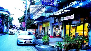 A street view with a parked car, a shop with a bright yellow sign, and potted plants in front. - Home at Samlan Soi 1 (Chiang Mai)