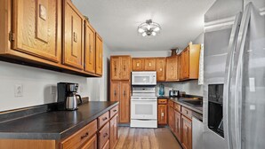 A kitchen with wooden cabinets, a stainless steel refrigerator, a white oven, and a black countertop. - Riley's Retreat  Hot Tub and air conditioning!   (Rapid City)