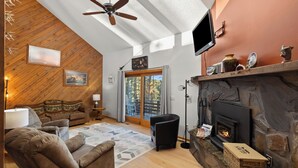 A cozy living room with a stone fireplace, wooden ceiling, and a large window. - Riley's Retreat  Hot Tub and air conditioning!   (Rapid City)