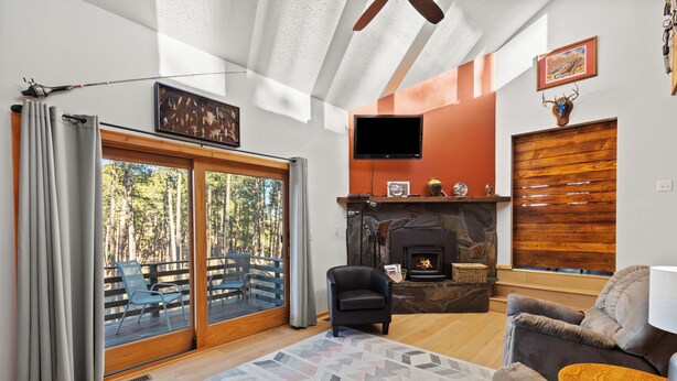 A living room with a fireplace, a television mounted on the wall, and a large window with curtains. - Riley's Retreat  Hot Tub and air conditioning!   (Rapid City)