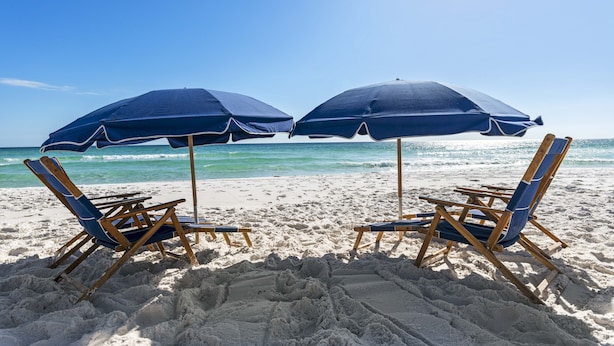 Zwei Liegestühle mit blauen Kissen und passende Sonnenschirme an einem Sandstrand.