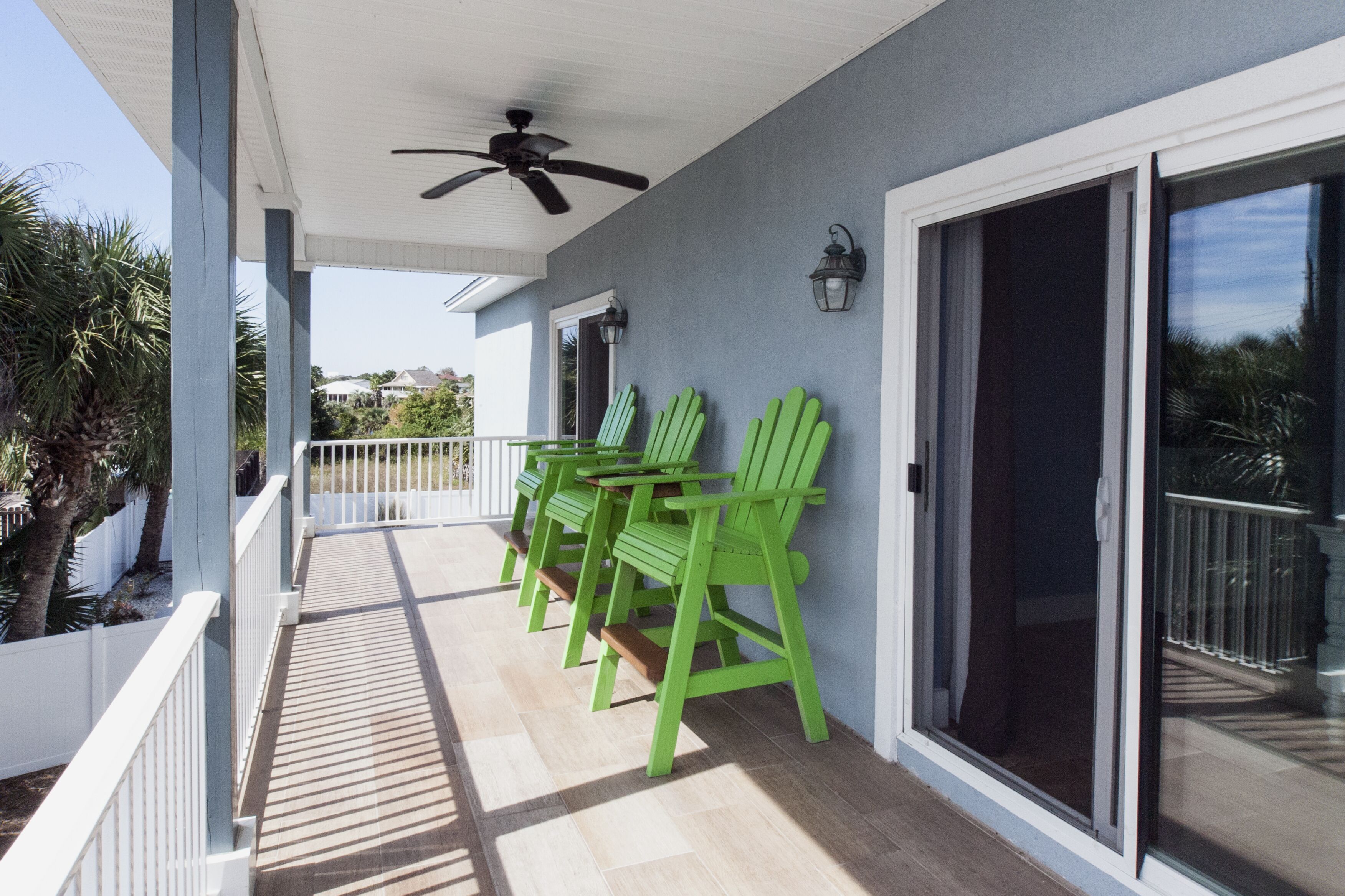 A covered outdoor area with a ceiling fan, a row of green chairs, and a sliding glass door.