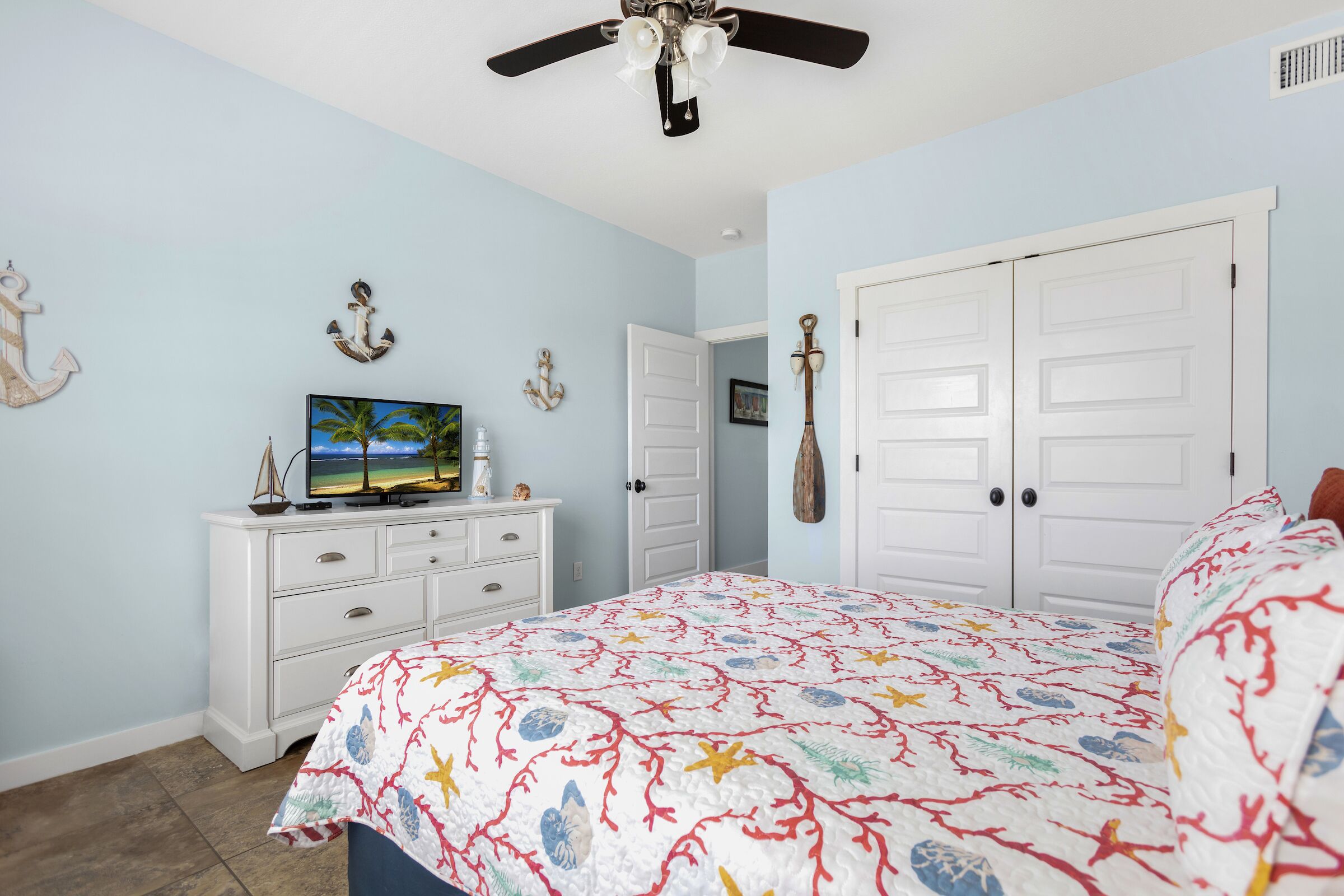 Un dormitorio con cama, cómoda, televisor y ventilador de techo.