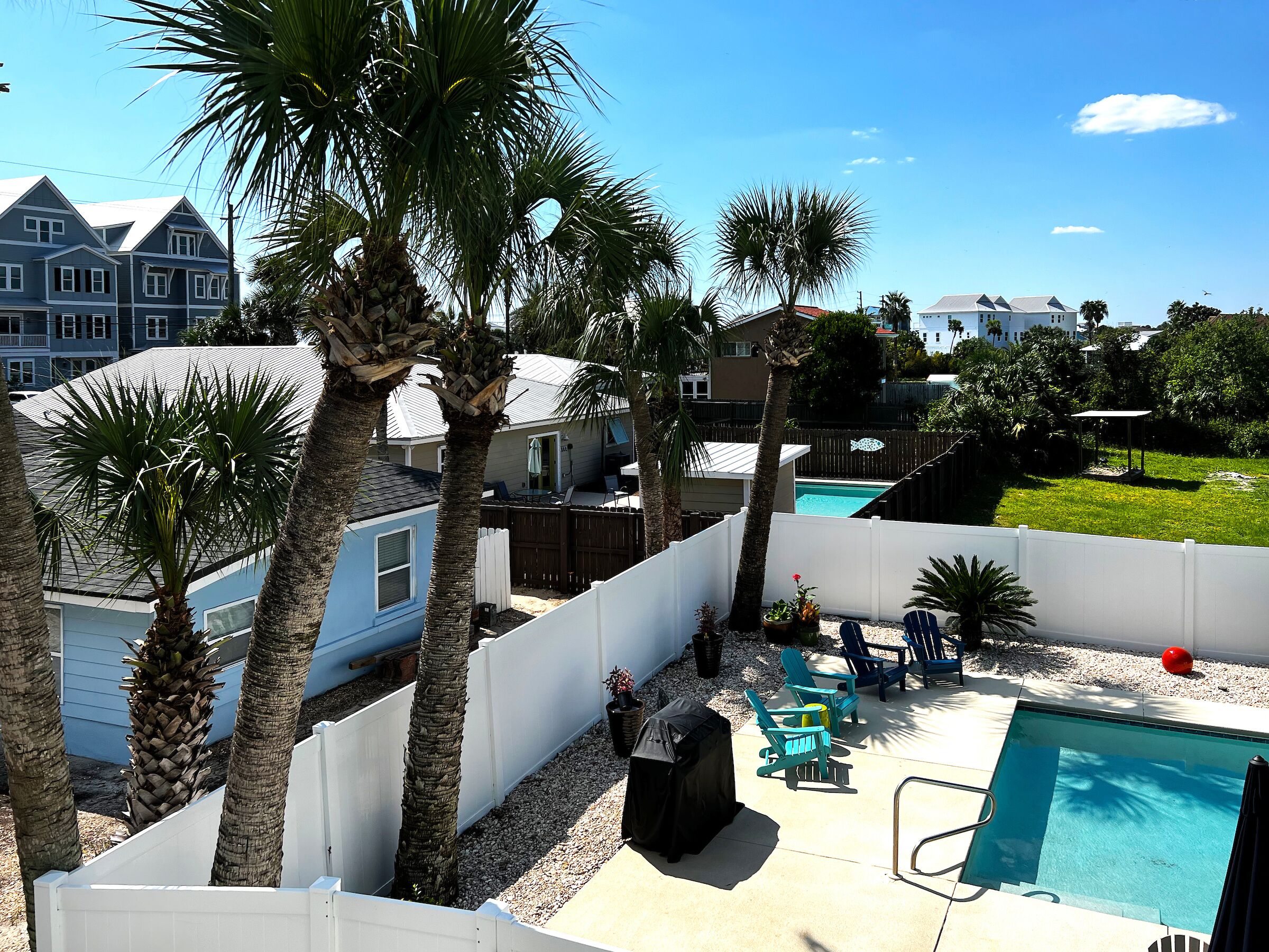 A backyard with a swimming pool, palm trees, and a fenced area.