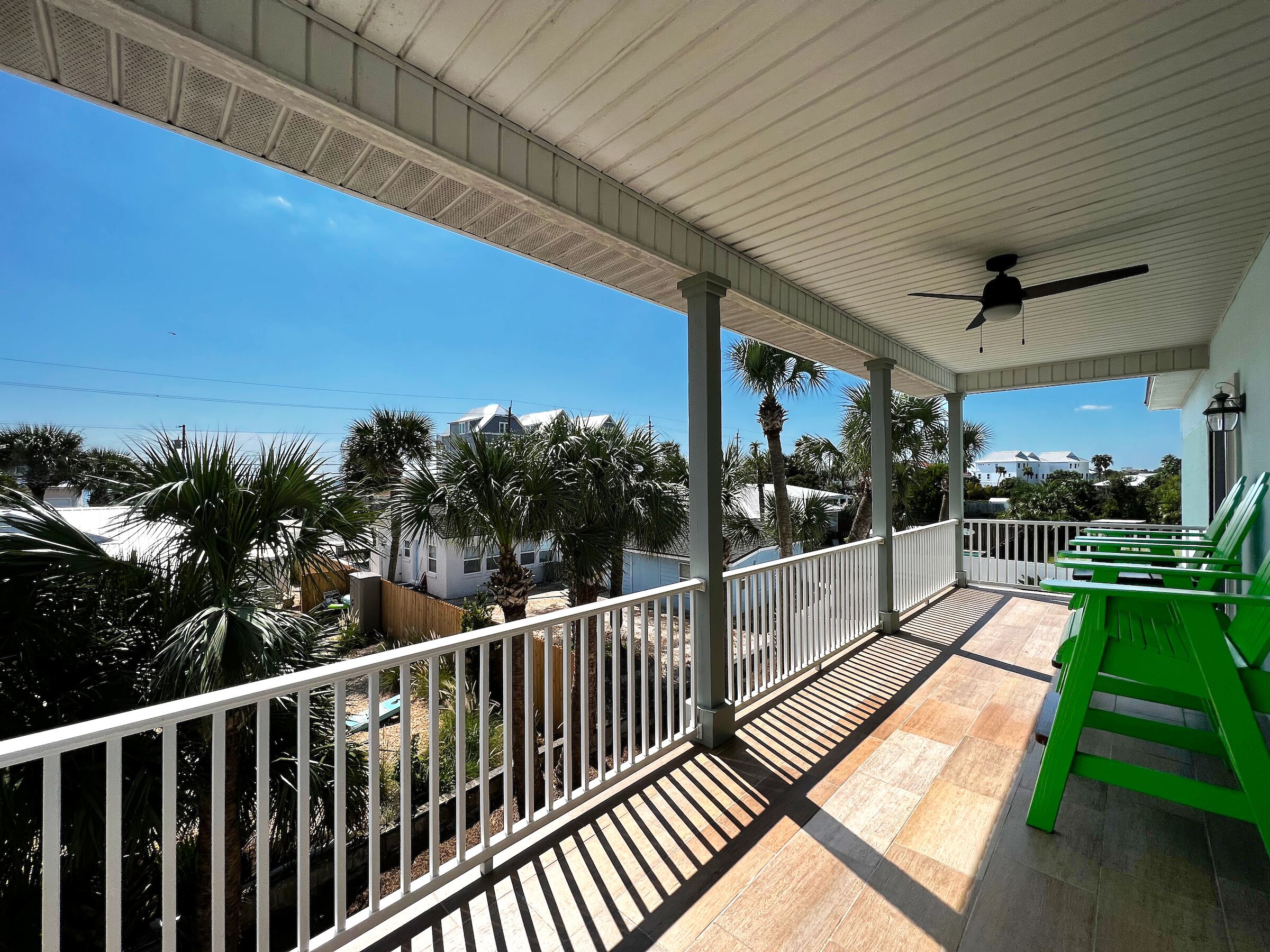 Een overdekt balkon met een plafondventilator, witte leuning en groene stoelen.