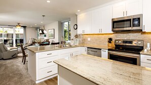 A modern kitchen with white cabinetry, stainless steel appliances, and a granite countertop. - Bright & Beautiful Ocean View 2BR Cottage with Stunning Upgrades (Oceanside)