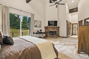 A bedroom with a bed, a fireplace, a television, and a large window.