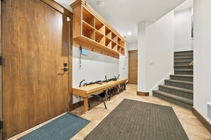 Un couloir avec une porte en bois, un banc avec des tuyaux, un radiateur fixé au mur et un escalier.