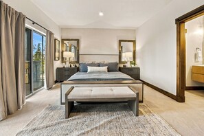 Une chambre à coucher avec un grand lit, un banc, une table de chevet, un miroir et une vue sur l’extérieur.
