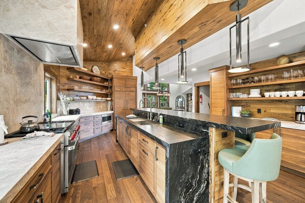 A modern kitchen with wooden cabinetry, a marble countertop, and a bar area with stools.