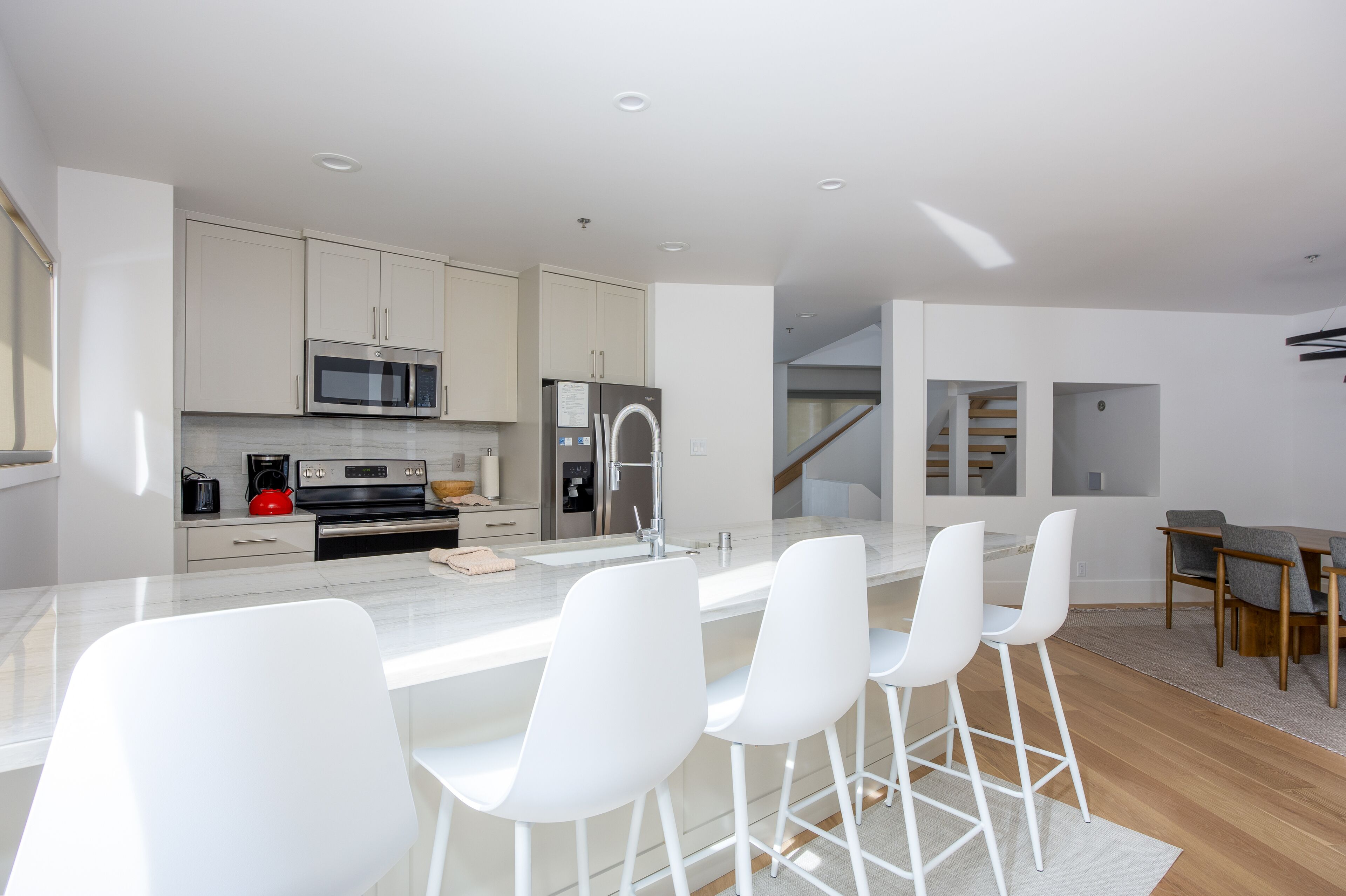 Een moderne keuken met witte kasten, roestvrijstalen apparatuur en een centraal eiland met barkrukken.