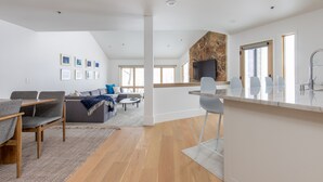 Uma cozinha moderna com painel de parede de pedra, uma sala de jantar com mesa e cadeiras de madeira, e uma sala de estar com sofá e mesa de centro.