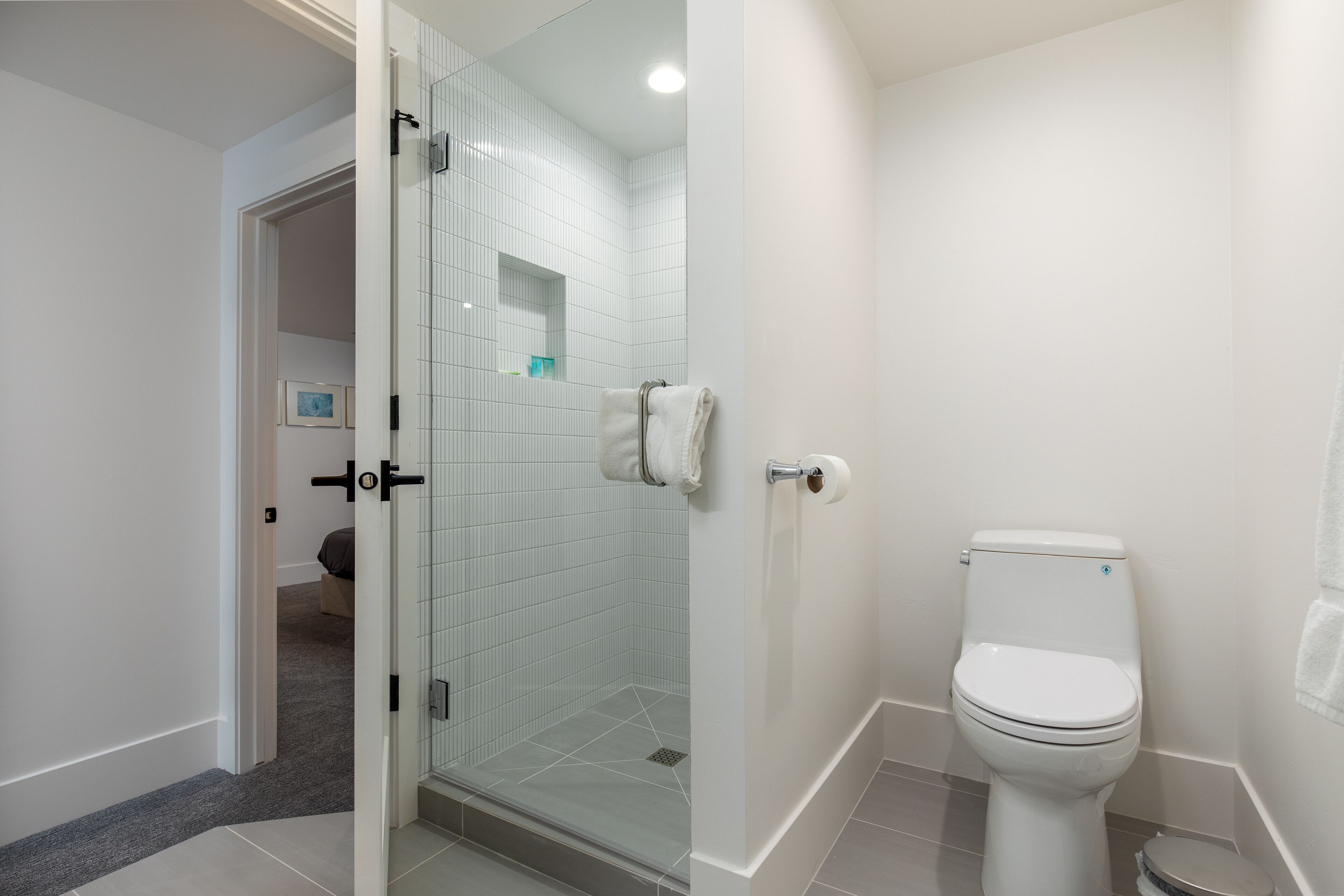 Ein modernes Badezimmer mit Duschkabine aus Glas, einer weißen Toilette und einem Handtuchhalter.